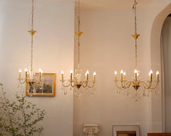 Three gold chandeliers hanging in a room with a neutral wall and decorative elements.