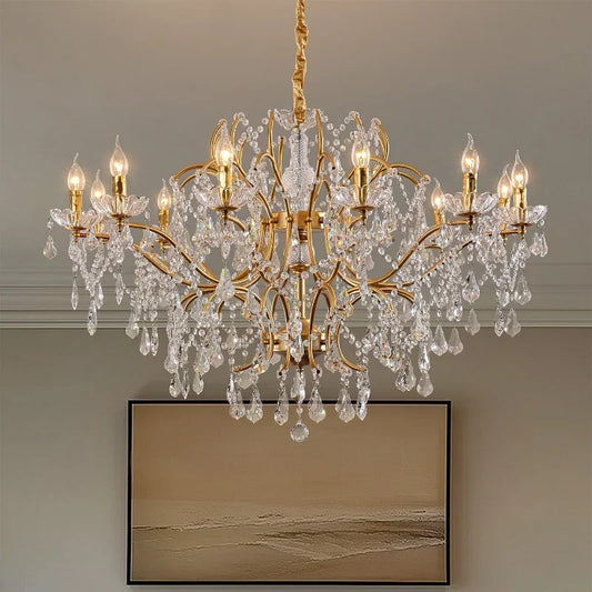 A grand gold chandelier adorned with numerous clear crystals, featuring candle-style light holders, suspended from a ceiling.