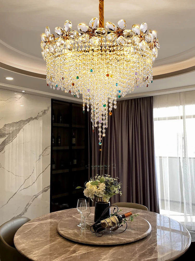 A grand gold chandelier with cascading crystals and petal details, suspended above a dining table setting.