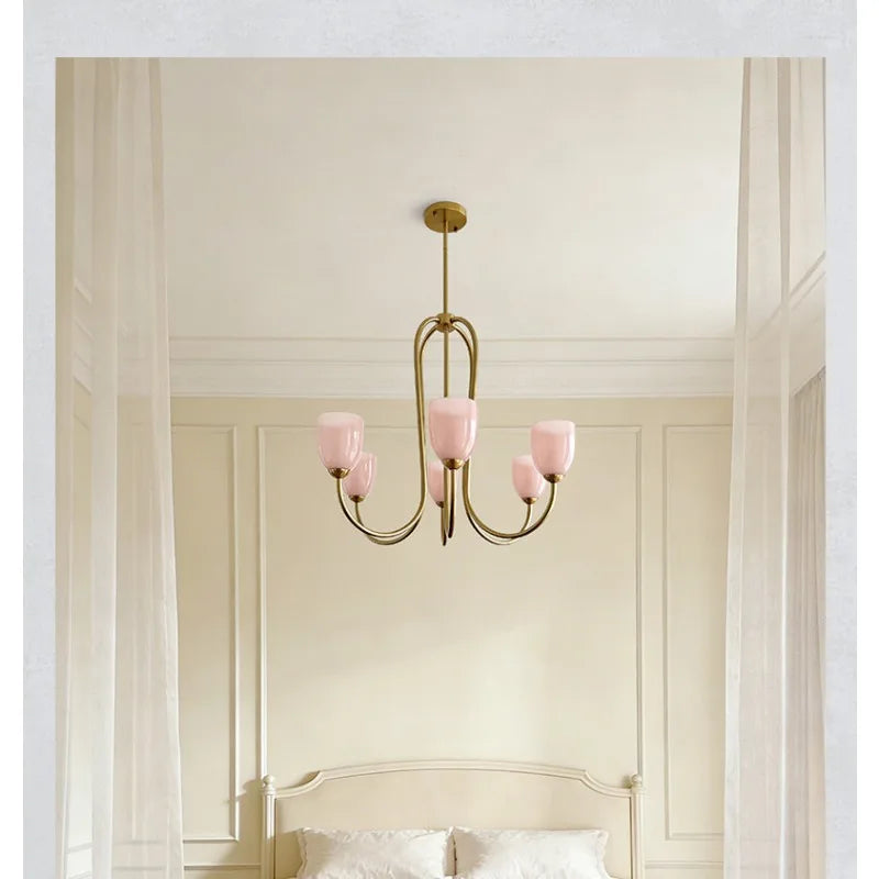 Brushed gold chandelier with pink tulip glass shades suspended over a bed.