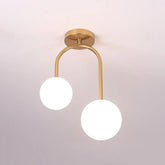 Close-up of a gold-finished semi-flush ceiling light with a U-shaped arm holding two white glass globes against a white ceiling.