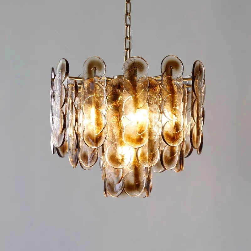 A pendant light with amber glass discs and a gold frame, shown against a neutral background.