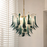 Close-up of a gold-tone tiered chandelier with cascading green and clear glass elements, illuminated by warm light.