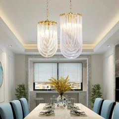 Two pendant lights, one gold and one chrome, with U-shaped clear glass tubes, hanging over a dining table.