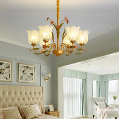 Gold floral chandelier above a bed in a bedroom setting with a large headboard and curtains.