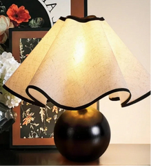 Decorative table lamp with a black base and beige shade on a surface.