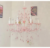A pink floral chandelier with crystal droplets and rose accents, illuminated against a white wall.