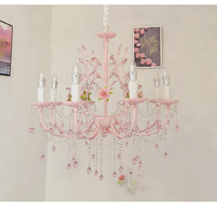 A pink floral chandelier with crystal droplets and rose accents, illuminated against a white wall.