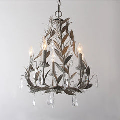 Grey wrought iron leaf chandelier with clear teardrop crystals hanging from candle-style lights, against a white background.