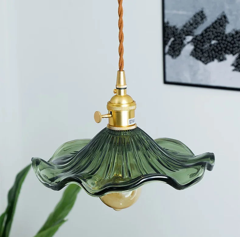 Green glass pendant light with gold fixture against a white wall
