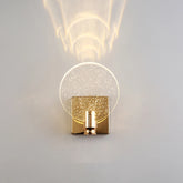 Close-up of a gold and clear bubble crystal wall sconce mounted on a white wall, showing its round shade and square base.