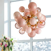 Gold glass ball cluster pendant light with frosted and clear orbs hanging near a window with a floral arrangement.