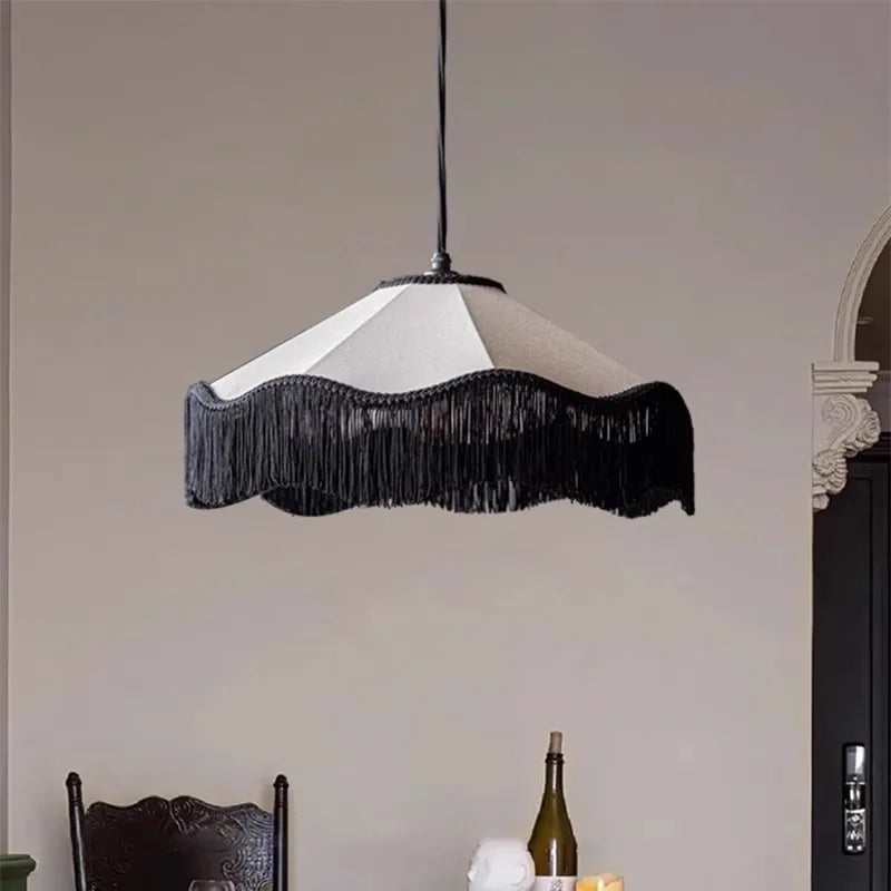 A black tassel fabric pendant light with a scalloped shade hanging above a dining area, with a bottle of wine visible in the foreground.