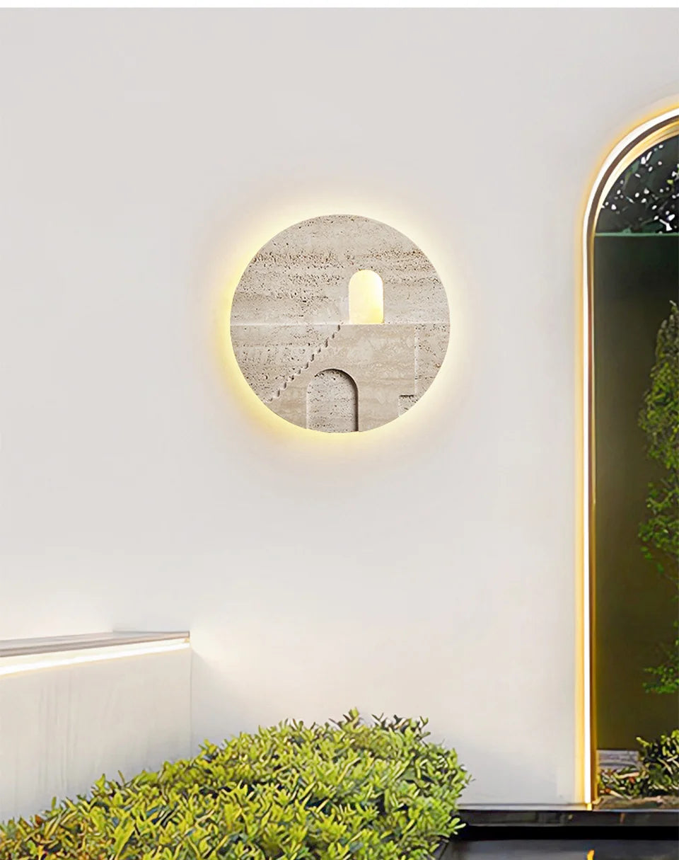 Round natural stone wall sconce with carved staircase and archway, illuminated by a warm glow around the exterior, mounted on a white wall.