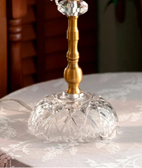 Decorative glass and gold candle holder on a lace tablecloth with flowers in the foreground.