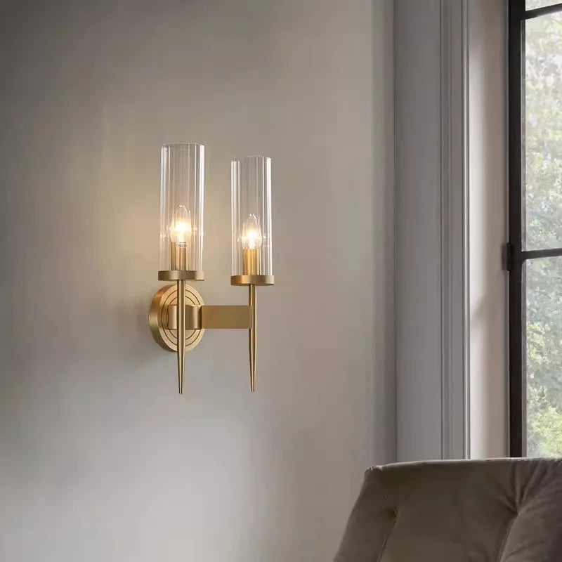 Gold wall sconce with clear glass shades on a neutral wall.