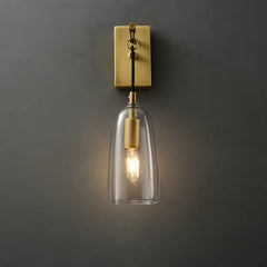 Front view of a gold and clear glass bell wall sconce against a dark gray wall, light illuminated.