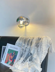 Decorative lamp on a wall with a magazine and lace fabric on a chair.