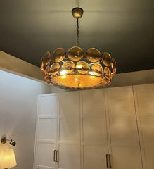 Gold chandelier hanging in a room with white cabinets and a lamp.