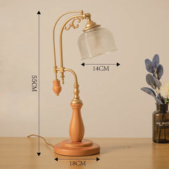 Table lamp with wooden base and gold metal arm, dimensions indicated, on a beige background.