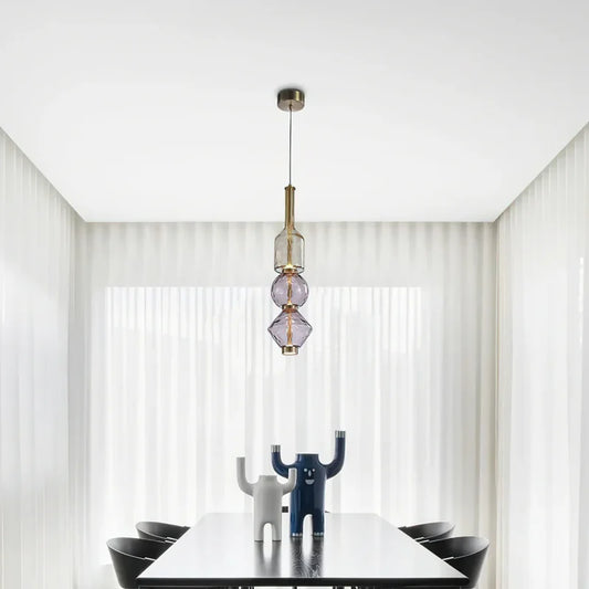 Modern pendant light with a clear glass orb shade and brushed gold hardware hanging over a dining table.
