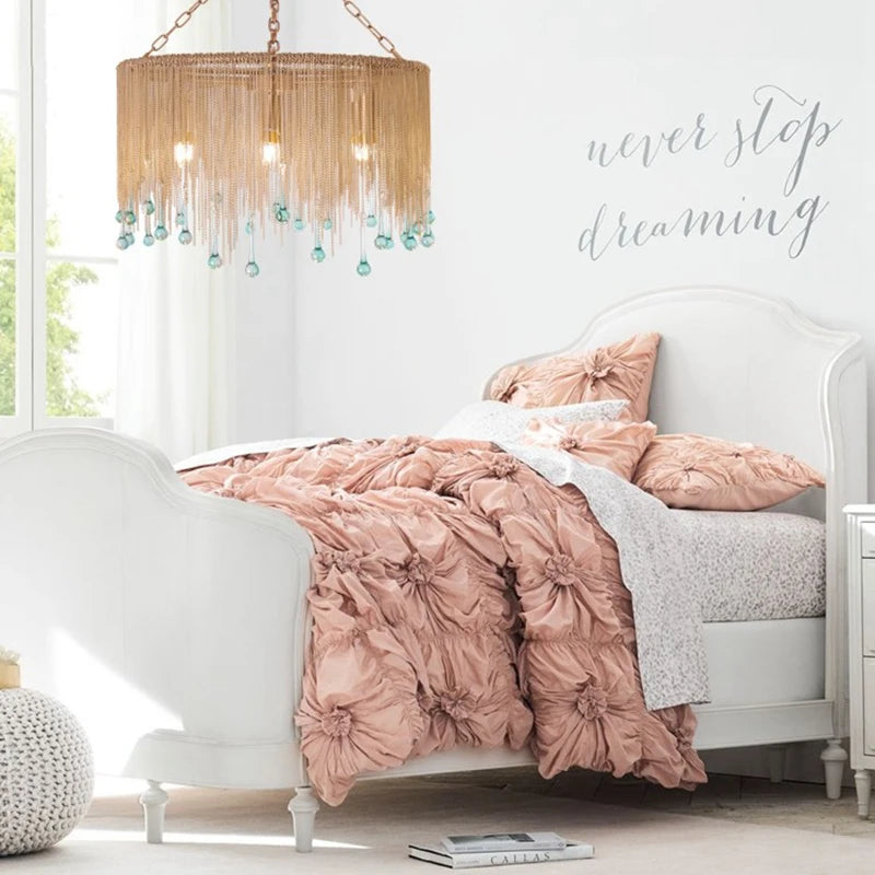 Gold chain tassel teardrop pendant light above a white bed in a bright room