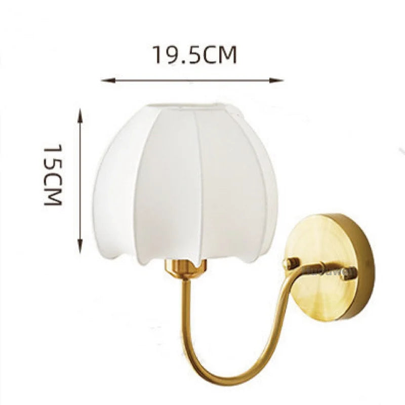 A gold wall sconce with a white pleated fabric shade shaped like a flower, with dimensions indicated: 19.5cm width and 15cm height.
