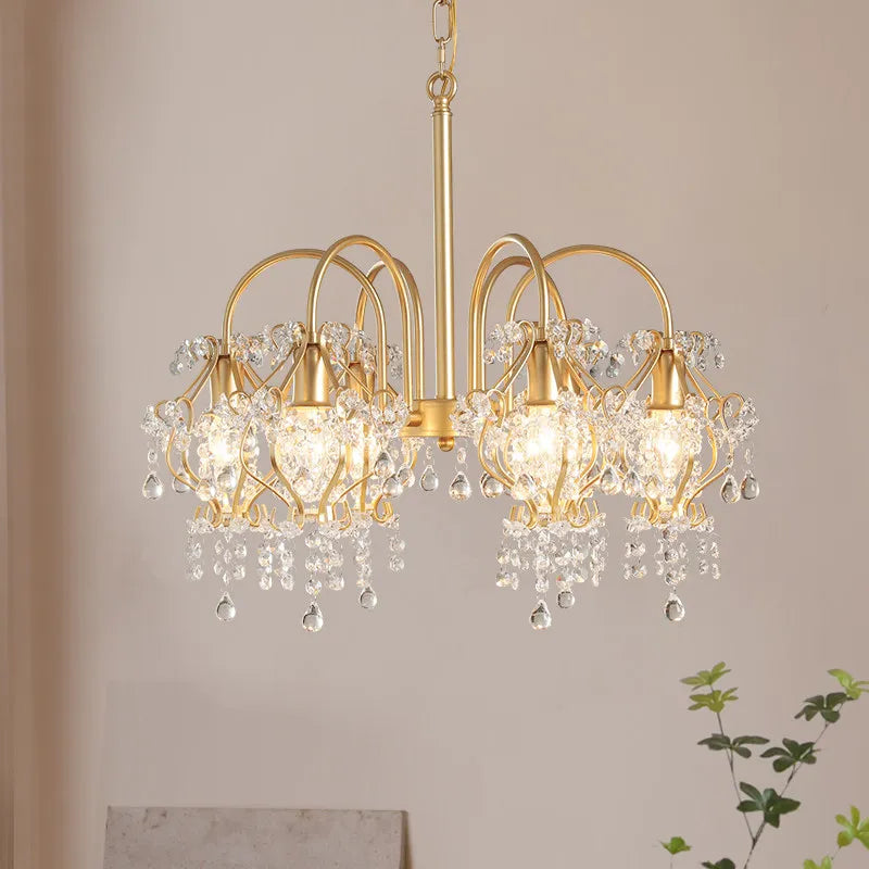 The gold crystal chandelier viewed from a side angle, showing the arrangement of the crystal strands and the overall silhouette.