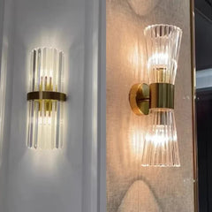 Two gold wall sconces with clear glass shades on a light gray wall.