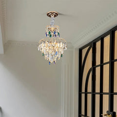 A gold multi-tier crystal chandelier with clear and colored crystals in a room with a black framed window.