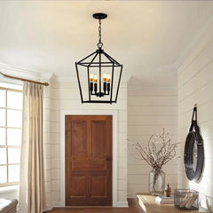 A black geometric cage pendant light hanging in a hallway with a wooden door and paneled walls.