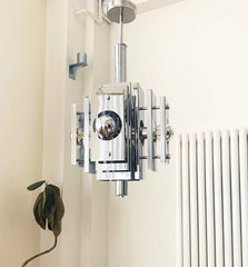 Modern chandelier hanging in a room with a radiator and plant.