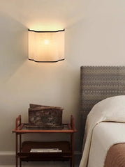 Wall-mounted light fixture above a wooden side table with a decorative box in a bedroom setting.