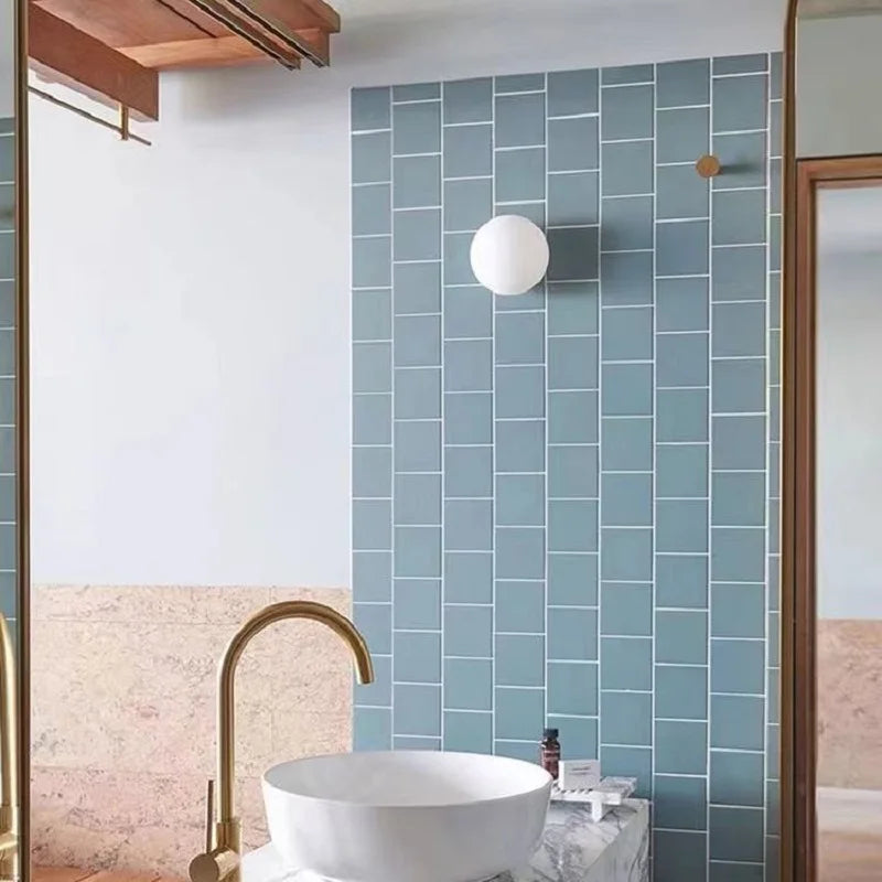 Bathroom with blue tiled wall, white sink, and gold faucet.