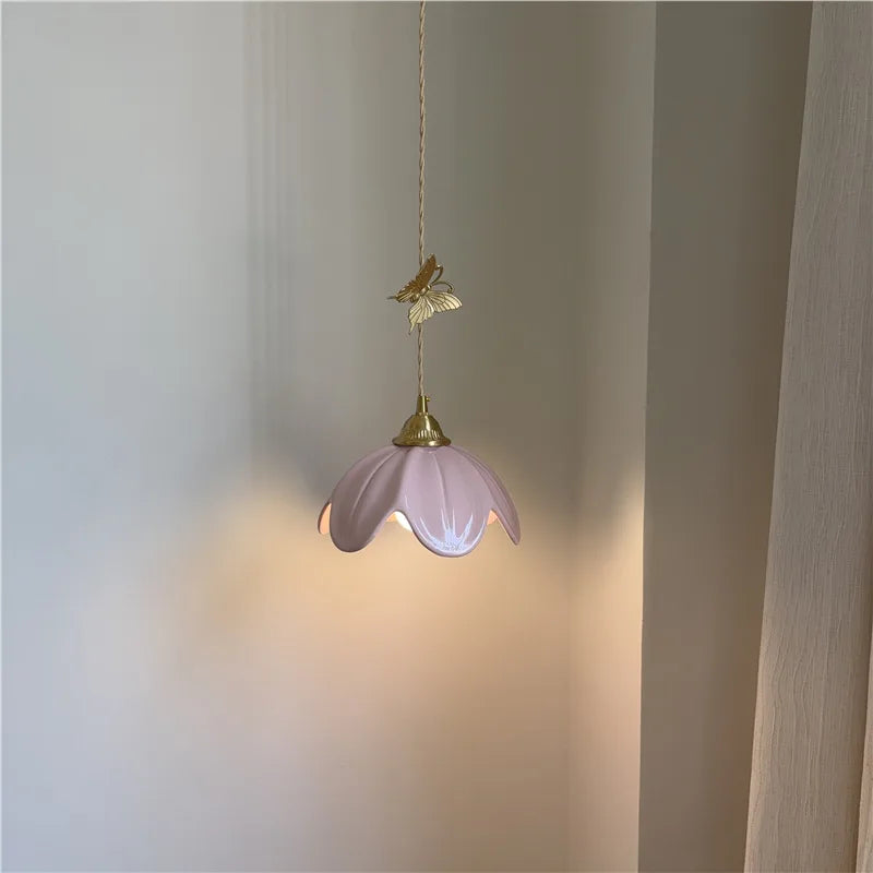 Pink ceramic petal pendant light with brass butterfly accent illuminated, casting a warm glow.