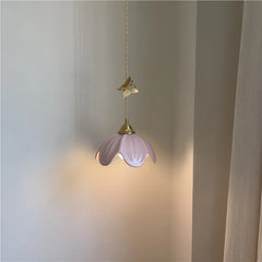 Pink ceramic petal pendant light with brass butterfly accent illuminated, casting a warm glow.
