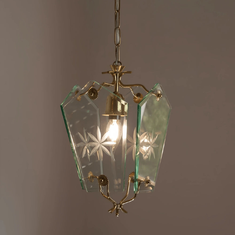 A clear glass pendant light with etched starburst patterns and brass accents, illuminated by a single bulb.