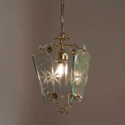 A clear glass pendant light with etched starburst patterns and brass accents, illuminated by a single bulb.