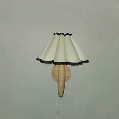Wall-mounted lamp with a wooden base and white lampshade on a plain wall.