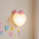 A pink bow heart-shaped wall sconce emitting a warm light, with cartoon stickers on the wall.