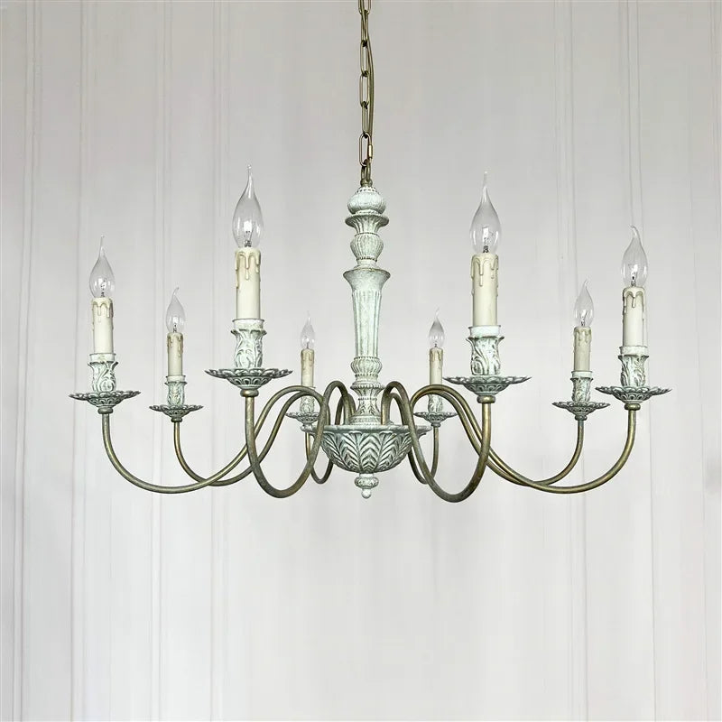 Vintage-style chandelier with multiple candle-like lights on a white paneled wall background.