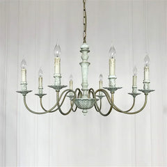 Vintage-style chandelier with multiple candle-like lights on a white paneled wall background.
