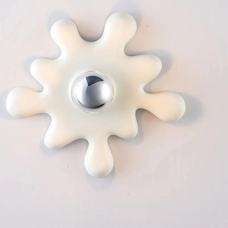 A white starburst shaped ceramic wall sconce with a chrome ball accent and a light bulb, mounted on a wall.