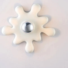 A white starburst shaped ceramic wall sconce with a chrome ball accent and a light bulb, mounted on a wall.