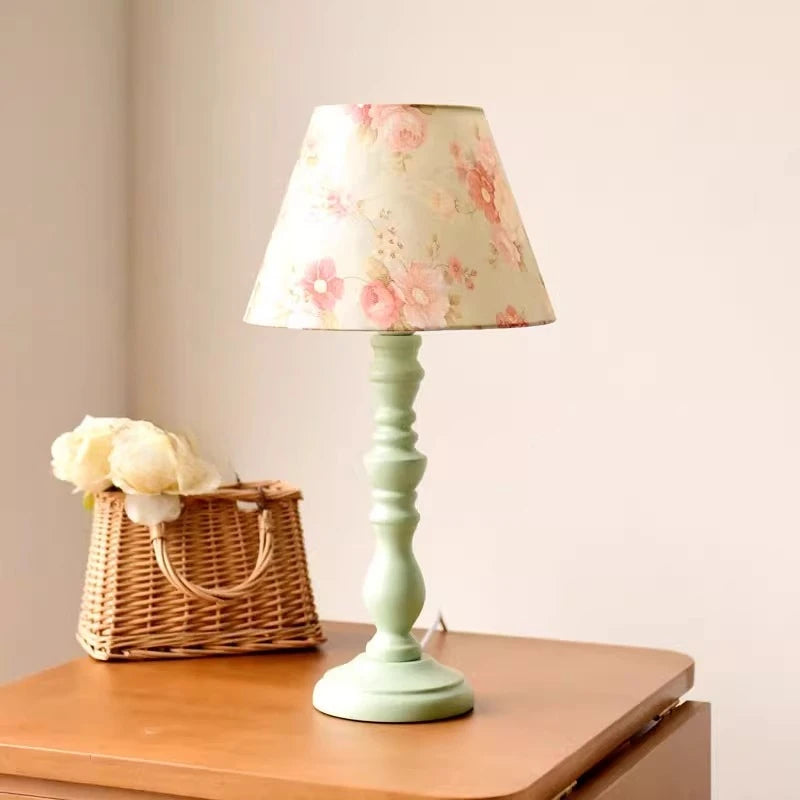 Floral-patterned lampshade on a light green base with a wicker basket and flowers on a wooden surface.