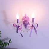 A purple wall sconce with two candle-style lights, decorated with purple bows and faux pearls, mounted on a light purple wall.