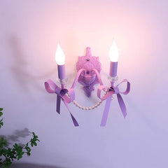 A purple wall sconce with two candle-style lights, decorated with purple bows and faux pearls, mounted on a light purple wall.