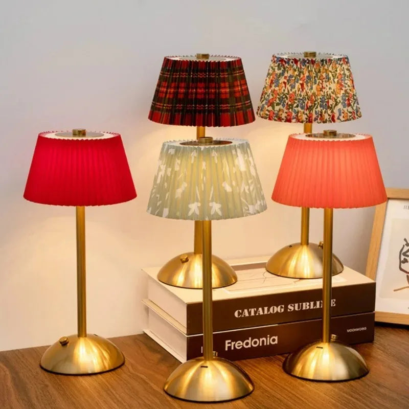 Four table lamps with different colored lampshades on a wooden surface.