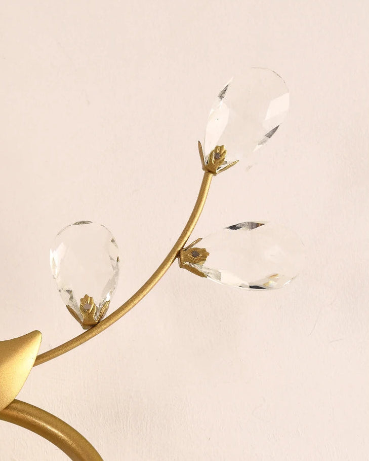 Decorative wall light fixture with gold arm and clea on a beige background