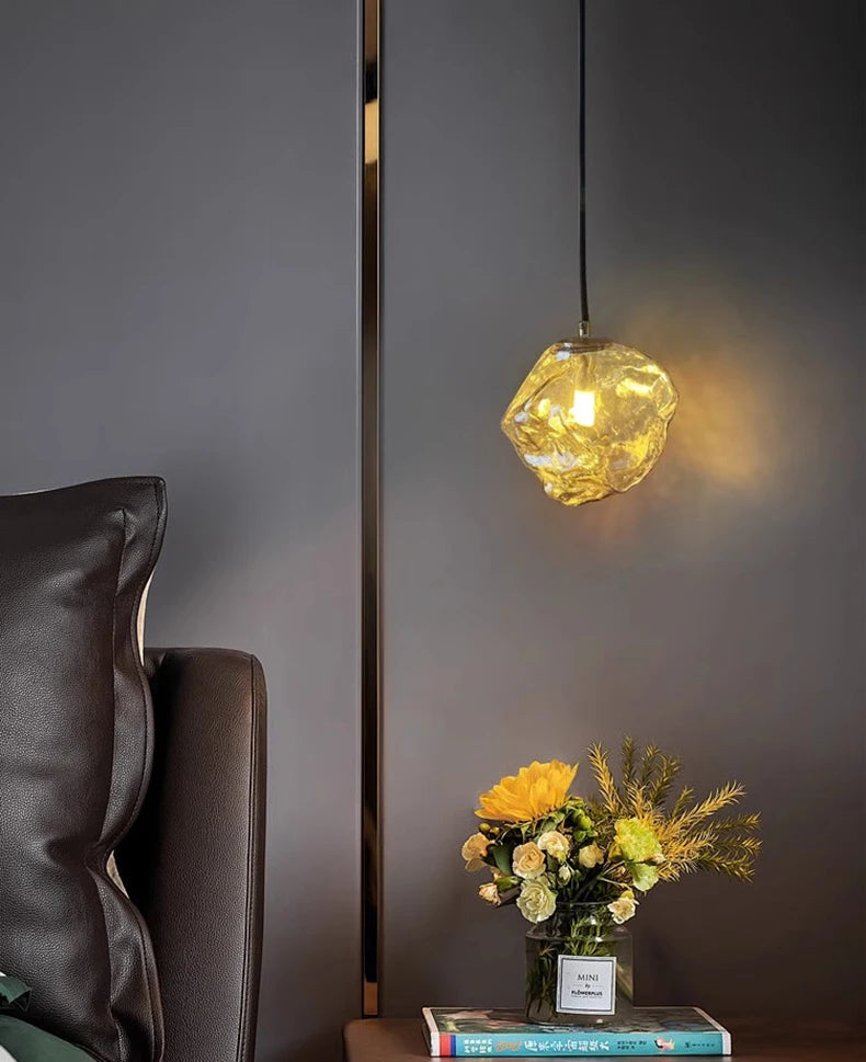 Geometric pendant light fixture casting a warm glow in a room with a dark gray wall, brown armchair, and a small table with flowers and books.